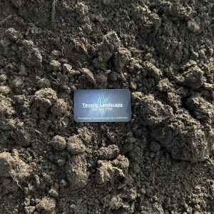 A business card for Tussis Landscape Ltd sits on uneven, dark brown soil with clumps and small ridges, highlighting the earthy texture and rough surface of the ground.