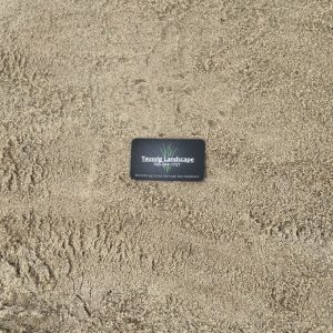 A black business card with the text "Talasek Landscape 512-944-7434, Everlasting Outdoor Living" lies on a sandy surface. The card features a small graphic of grass.