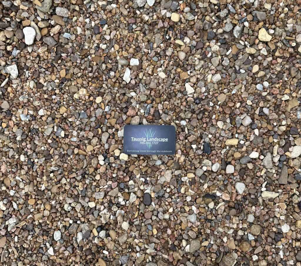 A black business card for Tranquil Landscapes lies on a surface covered with small, multicolored pebbles.